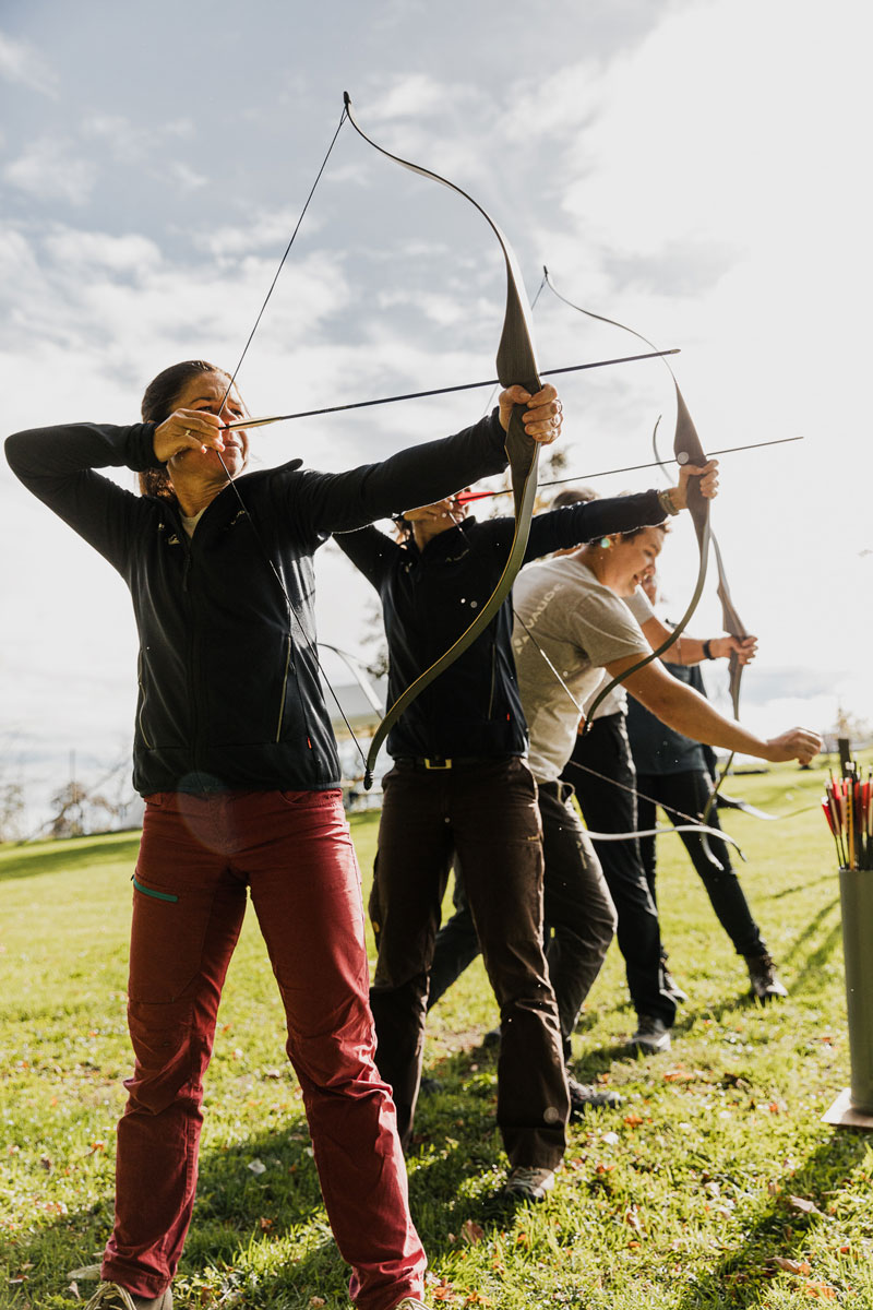 Frau zielt konzentriert mit einem langen Bogen auf eine Zielscheibe beim Intuitiven Bogenschießen